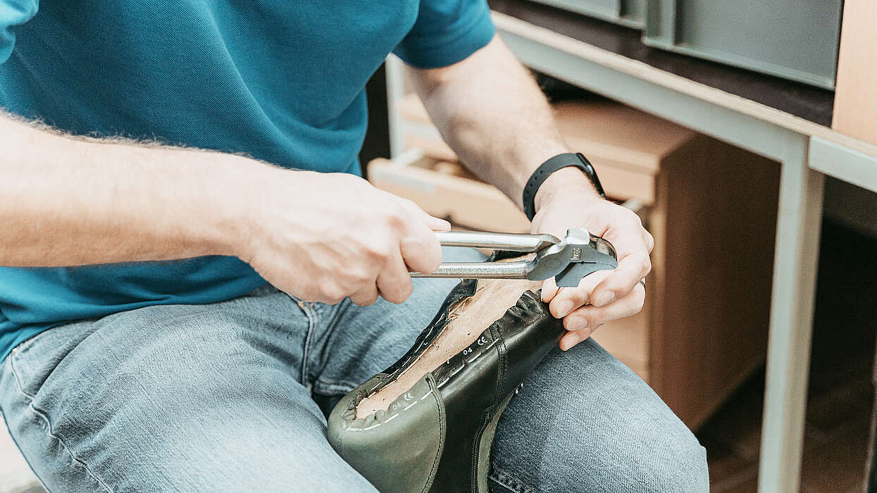 Ein Fachmann bearbeitet einen orthop&auml;dischen Schuh mit einer Zange, um Anpassungen vorzunehmen.